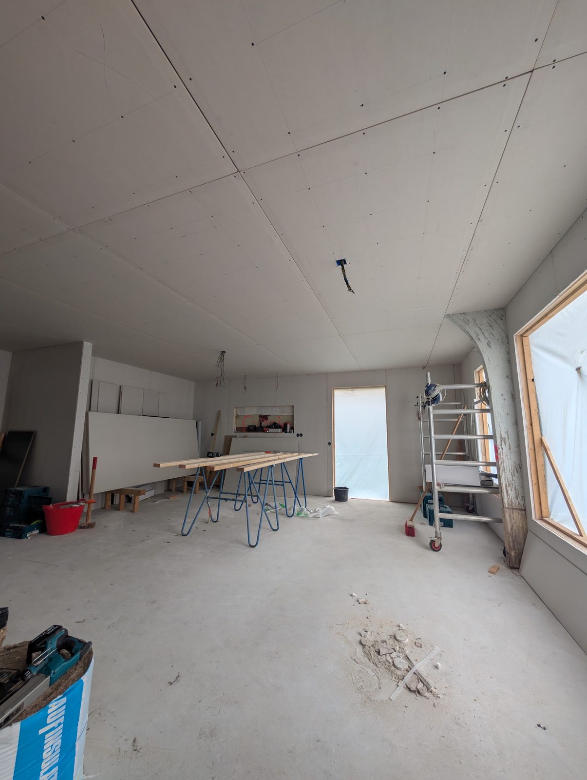 Een ruimte in aanbouw: gipsplaten plafond, schragen met planken en een trapje