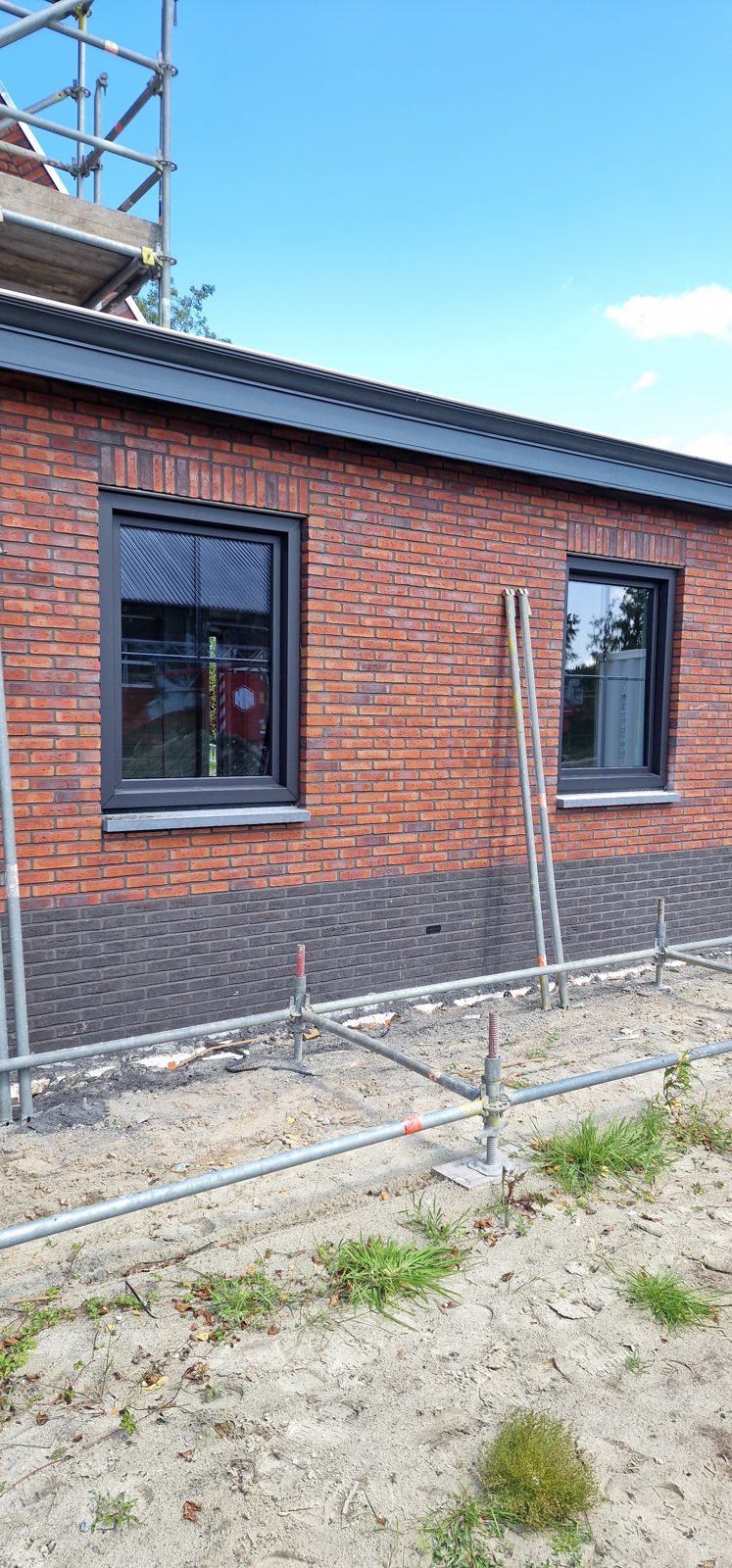 Een nieuwe woning in rode baksteen met zwarte kozijnen en een steiger